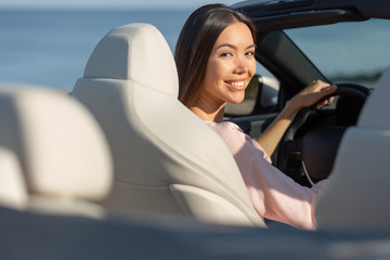 back view of smiling asian girl riding cabriolet and looking at the camera