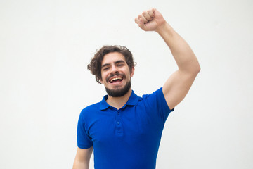 Happy excited guy making winner gesture, enjoying success. Handsome bearded young man in blue...