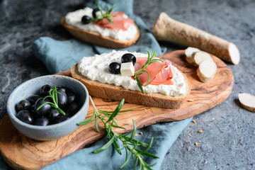 Slices of bread with creamy spread made from Feta cheese, horseradish and sour cream, served with Schwarzwald ham and black olives