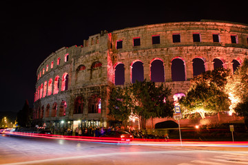 Fototapeta na wymiar Pula, Croatia / October 9th 2018: Pula Arena by night, long exposure of cars passing by and traffic lights in front of arena