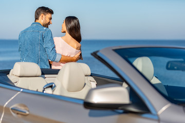 happy multiethnic couple hugging together with car on foreground