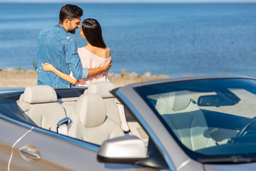 view of convertible with young couple hugging each other on the background