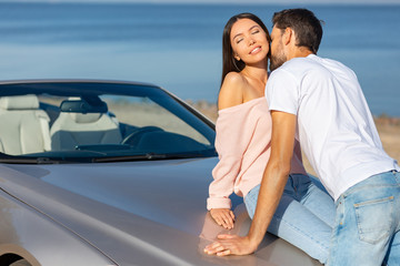 bearded man kissing his girlfriend leaning the car