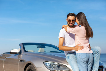 man looking at the camera while woman embracing him and leaning convertible