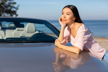 asian woman leaning convertible on the road