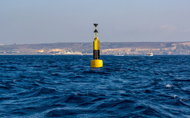 Yellow and black steel navigational floating buoy - West cardinal mark - in the blue Mediterranean sea water between Comino and Malta islands.