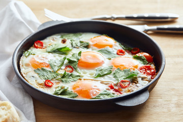 selective focus of fried eggs with parsley and chili pepper on wooden table with cutlery