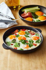 selective focus of fried eggs in frying pans at wooden table with cutlery, napkin and oil