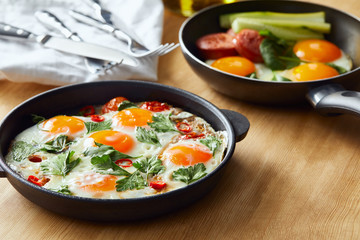 selective focus of fried eggs in frying pans at wooden table with cutlery, napkin