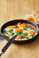 fried eggs with parsley and chili pepper on wooden table with cutlery and bread