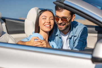 caucasian guy and asian woman sitting in convertible and hugging together