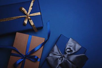 Three gift boxes wrapped in classic blue paper with a gold, blue and grey ribbons. Color of the year 2020, Classic Blue. Copy space.
