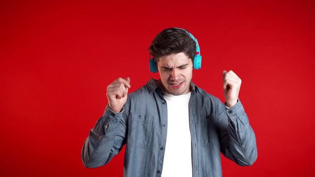 Handsome man with headphones dancing isolated on red background. Party, music, lifestyle, radio and disco concept.