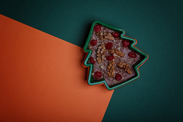 Handmade chocolate in the shape of a Christmas tree with cranberries and nuts on a green and orange background.