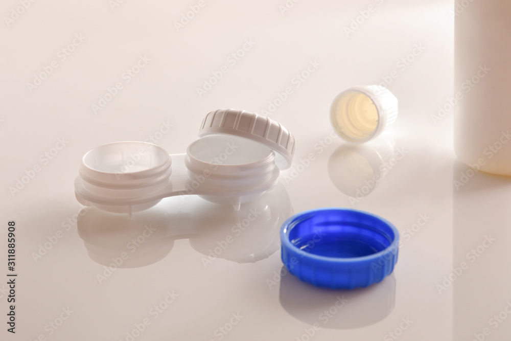 Wall mural Contact lens case and solution on white glass table