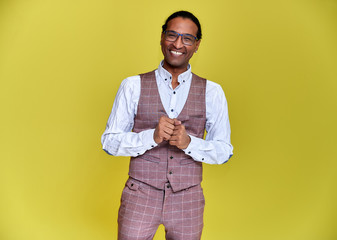 Portrait of a young African American man with short haircuts and a white-toothed smile in a business suit on a yellow background. Standing and talking right in front of the camera.