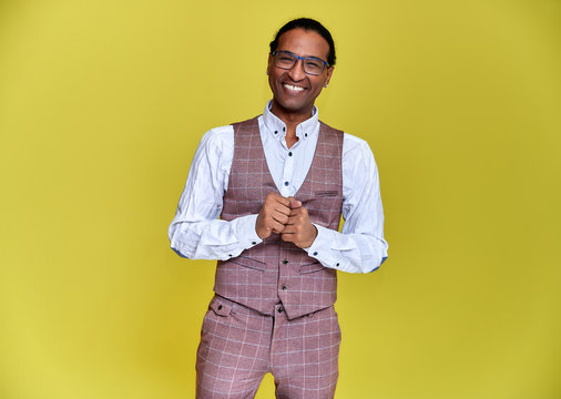 Portrait of a young African American man with short haircuts and a white-toothed smile in a business suit on a yellow background. Standing and talking right in front of the camera.