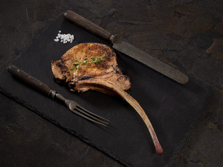 grilled pork steak tomahawk on black slate on a dark background