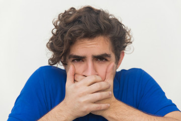 Closeup of stressed guy covering mouth with both hands. Handsome bearded young man in blue casual t-shirt posing isolated over white background. Feeling sick concept