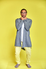 Vertical portrait of a cheerful young man wearing glasses African-American with a short haircut in ordinary clothes on a yellow background in full length. Standing right in front of the camera