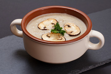 Cream soup with mushrooms in porcelain bowl on black background.