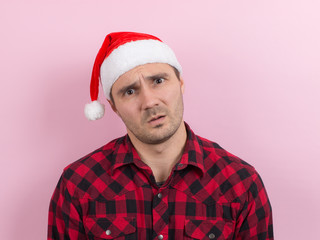 Emotions on the face, indifference and disgust. A man in a plaid rabbit and a Christmas red hat, on a pink background, copy space.