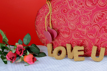 A beautiful red and gold candy box on a white table with a red background. Cork letters spell the words love u for Valentine's Day in February