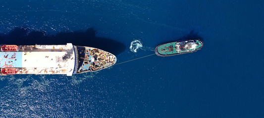 Aerial drone ultra wide photo of industrial tug assisting boat ass in deep blue Mediterranean sea