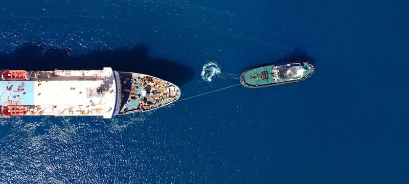 Aerial drone ultra wide photo of industrial tug assisting boat ass in deep blue Mediterranean sea