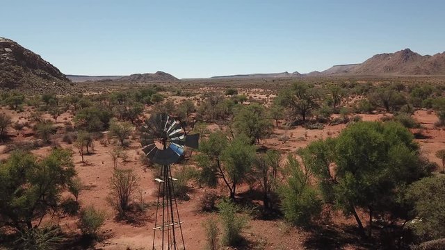 4K aerial drone video of farm wind water pump on pillar, red stone gravel plains, wide dry bush savanna panorama near town Grunau, Namibia, B1 desert highway near RSA border, southern Africa