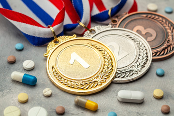 Doping for athletes. Gold, silver and bronze medal and pills with capsules on a gray background