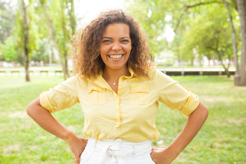 Outdoor portrait of positive joyful woman in summer park with green grass in background. Curly haired black woman in casual posing outdoors. Happy woman outside concept