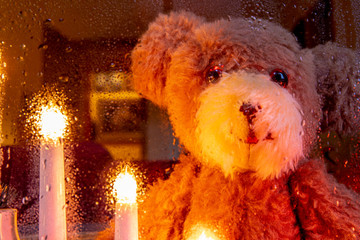 A window is festively decorated for Christmas. A teddy looks through the rain-soaked window pane....