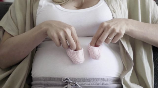 Pregnant woman playing with babys bootees on belly. Focused future mother looking at belly. Pregnancy concept