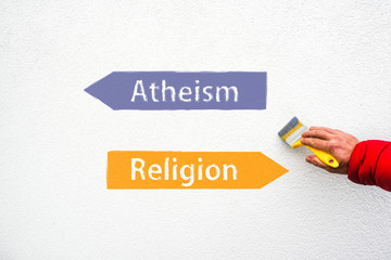 arrow signs of words atheism and religion on wall and hand with paint brush
