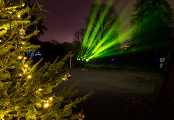 Christmas toys, burning yellow bulbs on a Christmas tree in the park against the background of green rays of spotlights, in the winter evening.