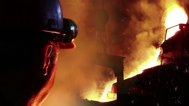 Liquid metal in the foundry, melting iron in furnace, steel mill. Worker with goggles and helmet controlling iron smelting in furnaces. Applying heat to ore in order to extract a base metal