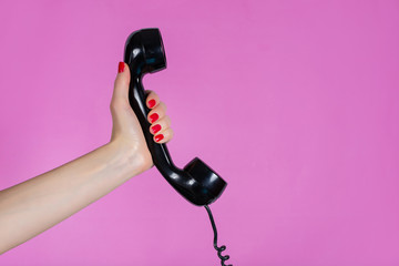 Female hand holding old and retro telephone headset isolated on pink background in studio. Girl hands with red manicure on fingers. Minimalism and retro concept - Powered by Adobe
