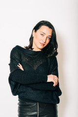 Studio portrait of beautiful brunette woman wearing black pullover, posing on white background, arms crossed