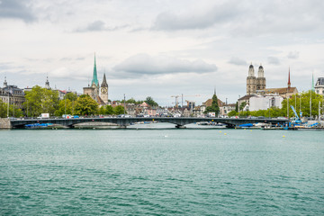 Obraz premium View of the historic buildings and bridge of Zurich at the bank of Limmat River and Zurich lake, with landmark of Fraumünster Church clock tower, Grossmunster (Great Church) and church tower of St. P