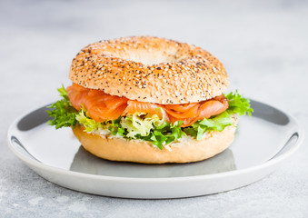 Fresh healthy bagel sandwich with salmon, ricotta and lettuce in grey plate on light kitchen table background. Healthy diet food.