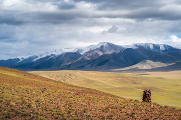 Fototapeta na wymiar Cairn on a hillside. On the horizon is the Chikhachev Ridge, the border between Russia and Mongolia. Autumn. Kosh-Agach district, Altai Republic