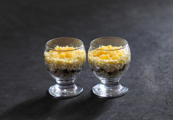 Layered salad of chicken, mushrooms, cheese, eggs and pineapples in a glass on a dark gray background