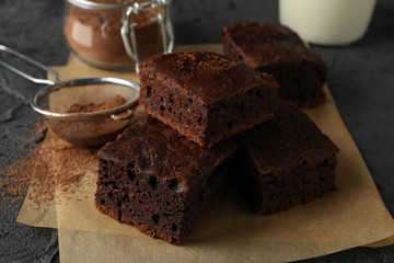 Chocolate cake slices, bottle of milk and strainer with powder on black background, close up