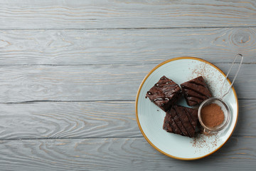 Plate with chocolate cake slices and strainer with powder on wooden background, space for text