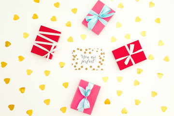 Valentines day background with paper card, gift box and golden heart confetti on white. Flat lay