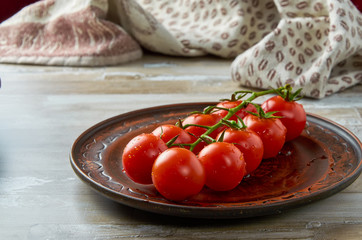 Cherry tomatoes on a green branch lie in a brown clay plate with drops of water. Close-up.
