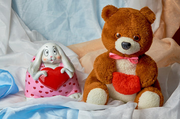 A teddy bear with a red heart in his hands, and a bunny with a heart in his hands on a colored holiday background with place for text. Valentine's Day. Postcard.8 March