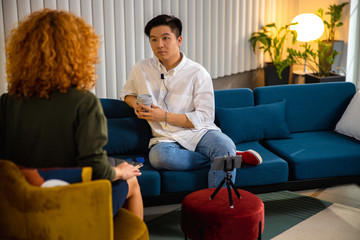 Obraz premium Asiam man sitting on sofa and holding hot drink