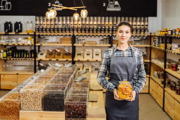 A midsection of a shop assistant in a zero waste shop, holding a jar with groceries.